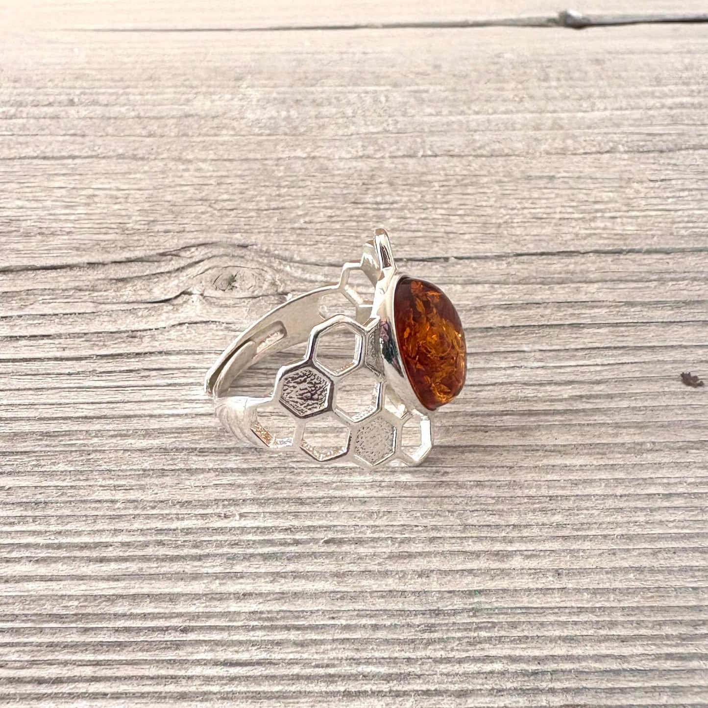 Silver ring with honeycomb design and amber stone on a wooden surface