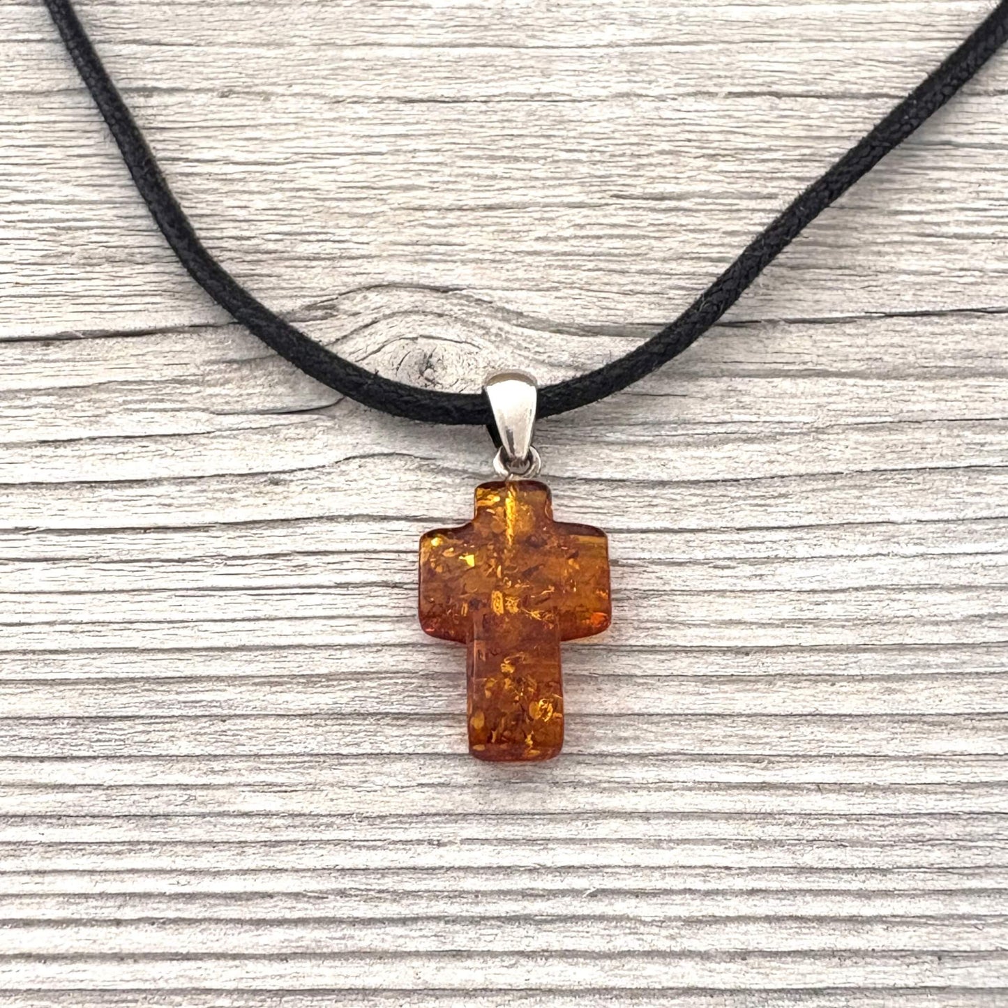 Amber cross pendant on a black cord against a wooden background