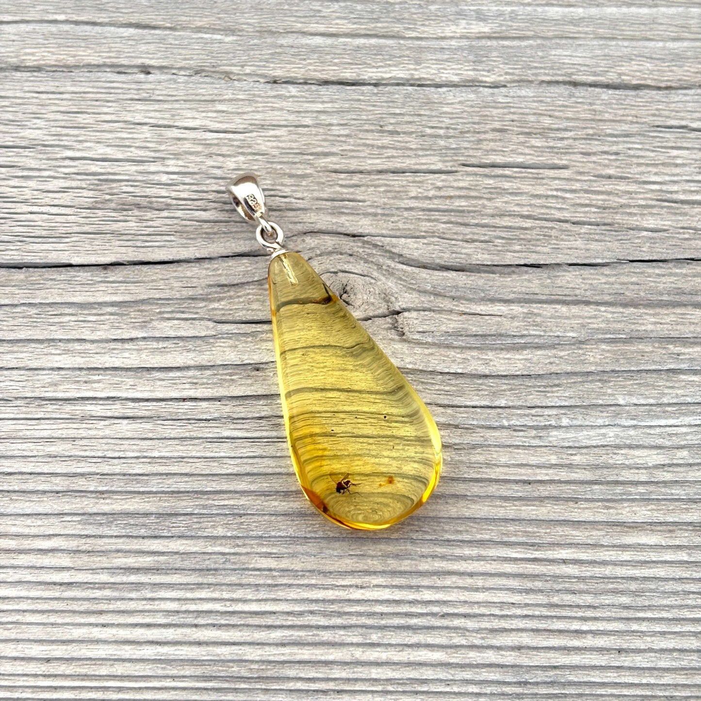 Teardrop-shaped amber pendant with insect on a wooden surface