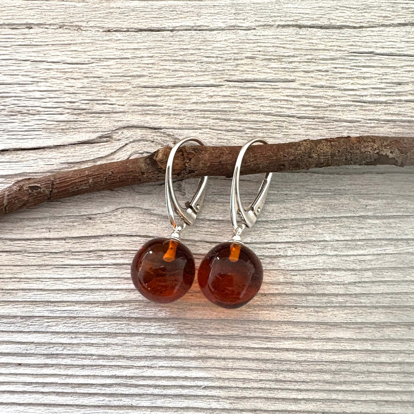 Pair of amber earrings on a wooden branch with a wooden background