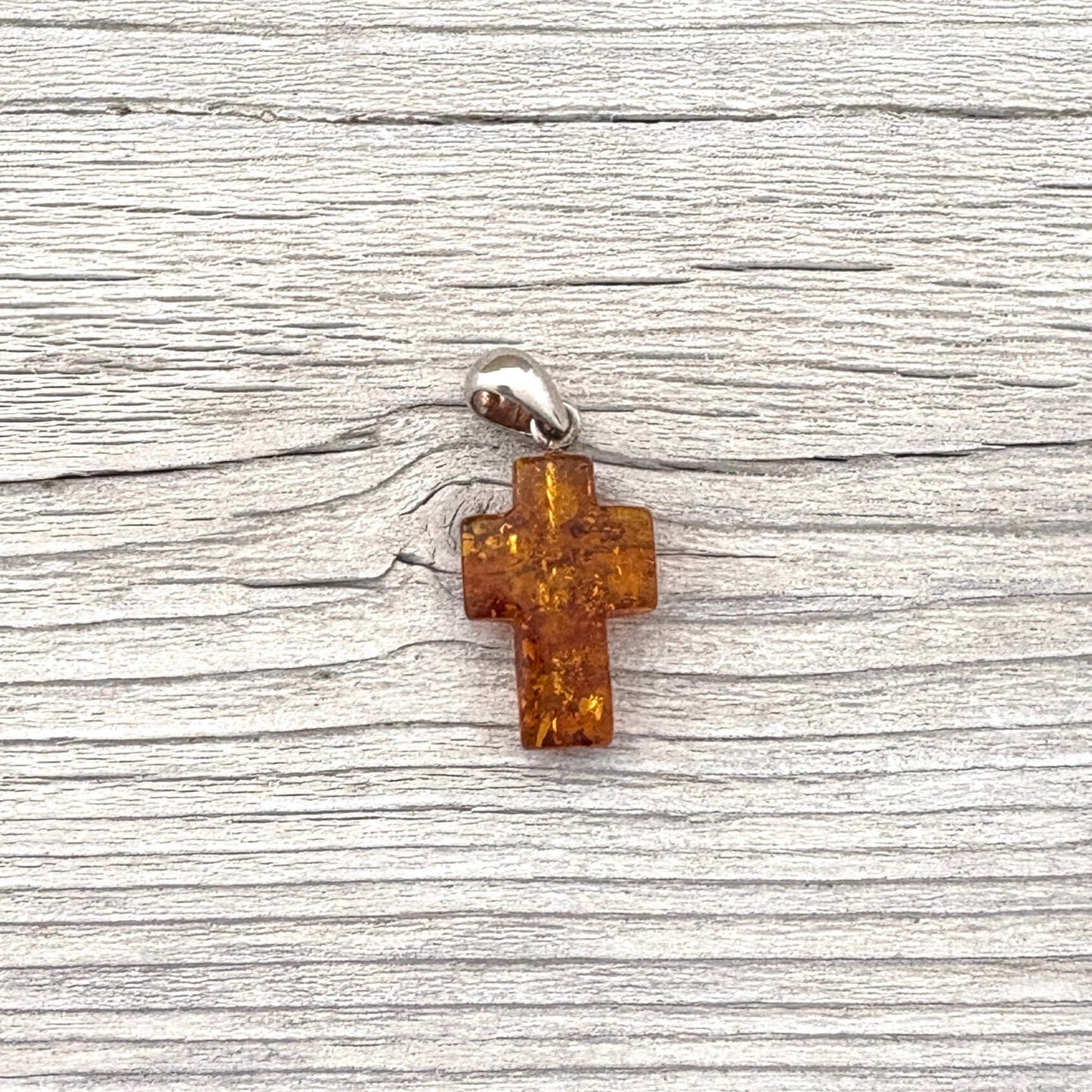 Amber cross pendant with a silver bail against a wooden background