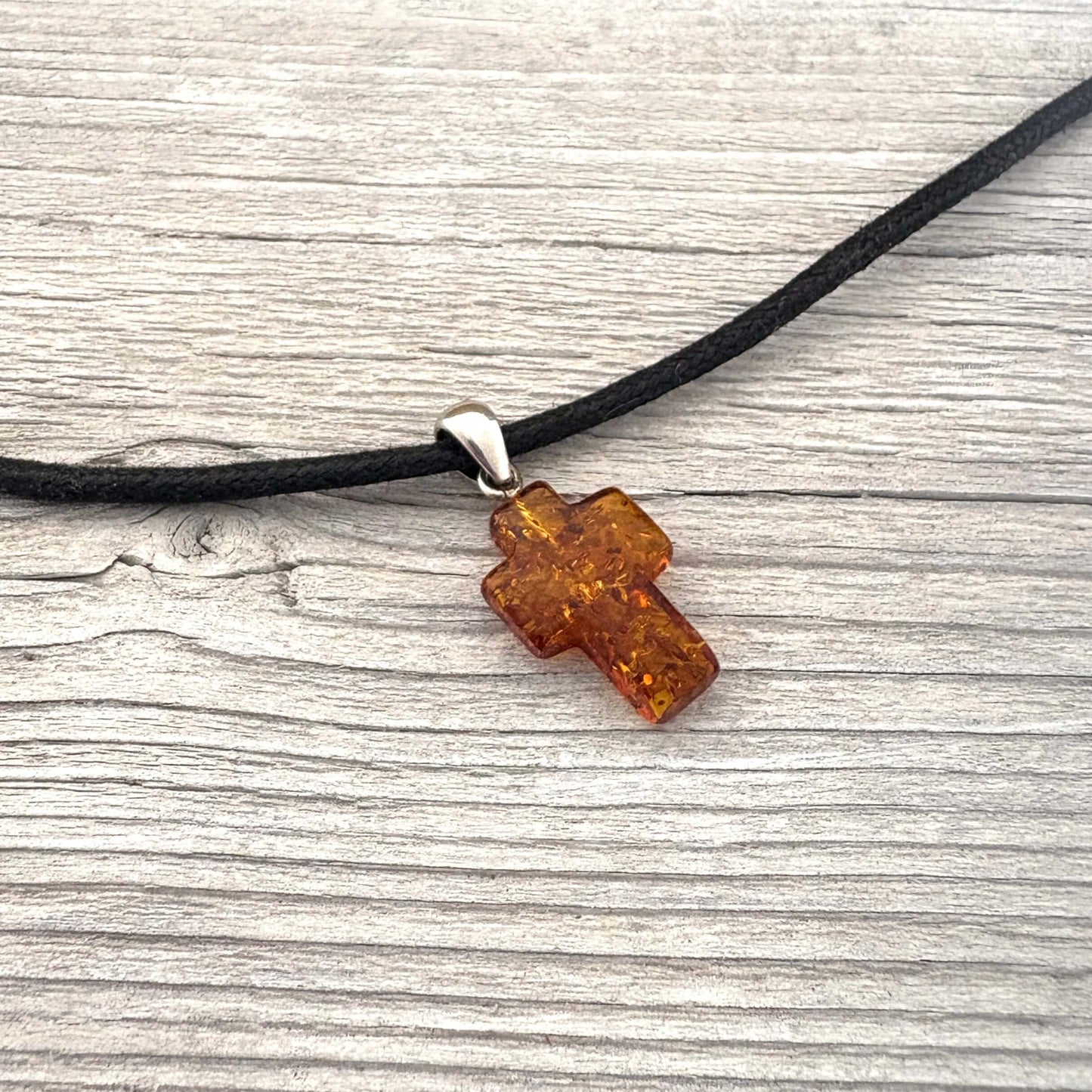 Amber cross pendant on a black cord against a wooden background