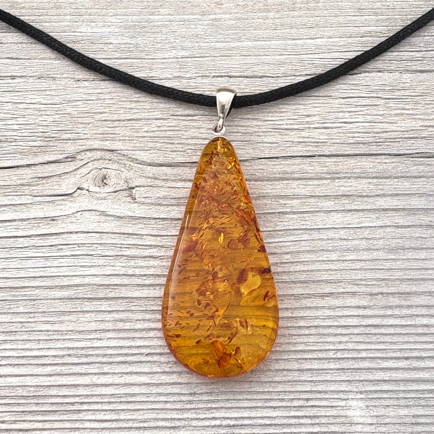 Teardrop-shaped amber pendant on a black cord against a wooden background