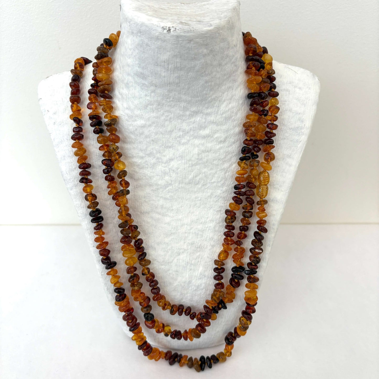 Long amber bead necklace on a white mannequin bust.