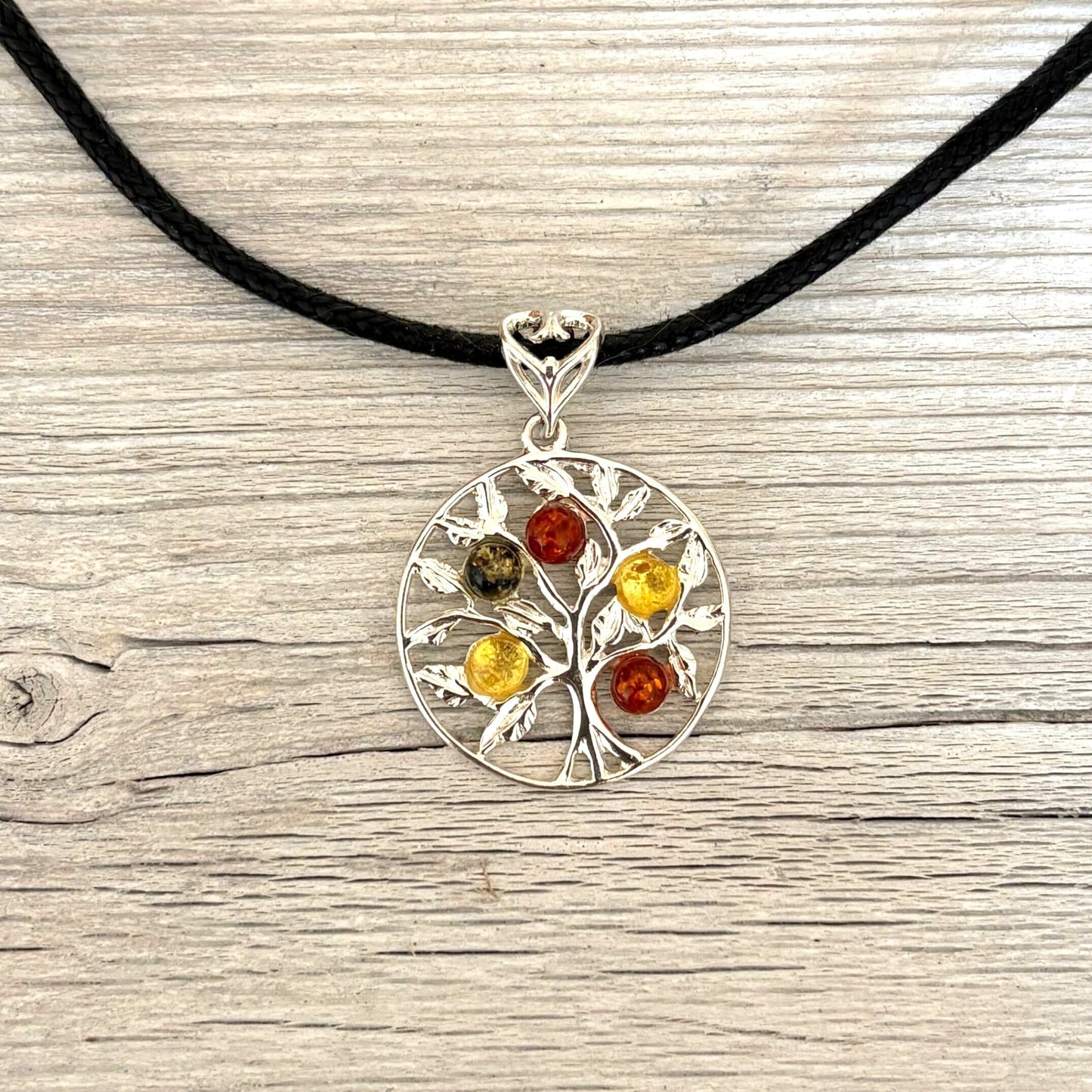 Silver and amber pendant with colored stones on a black cord against a wooden background