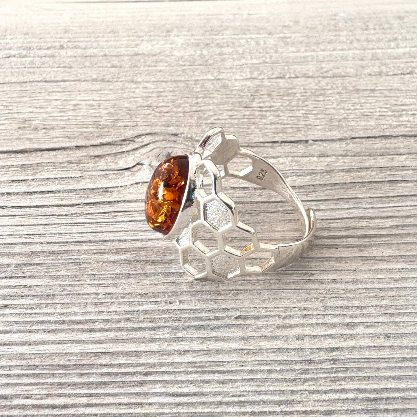 Silver ring with a honeycomb design and amber stone on a wooden surface