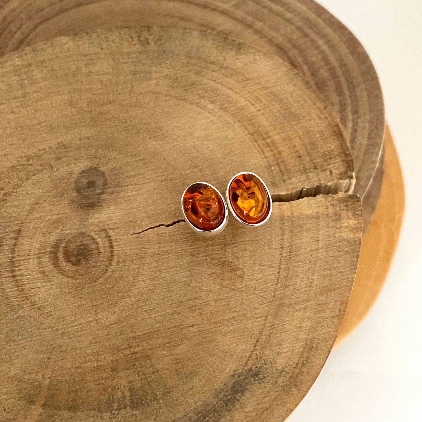 Pair of oval shaped amber stud earrings on a wooden surface front