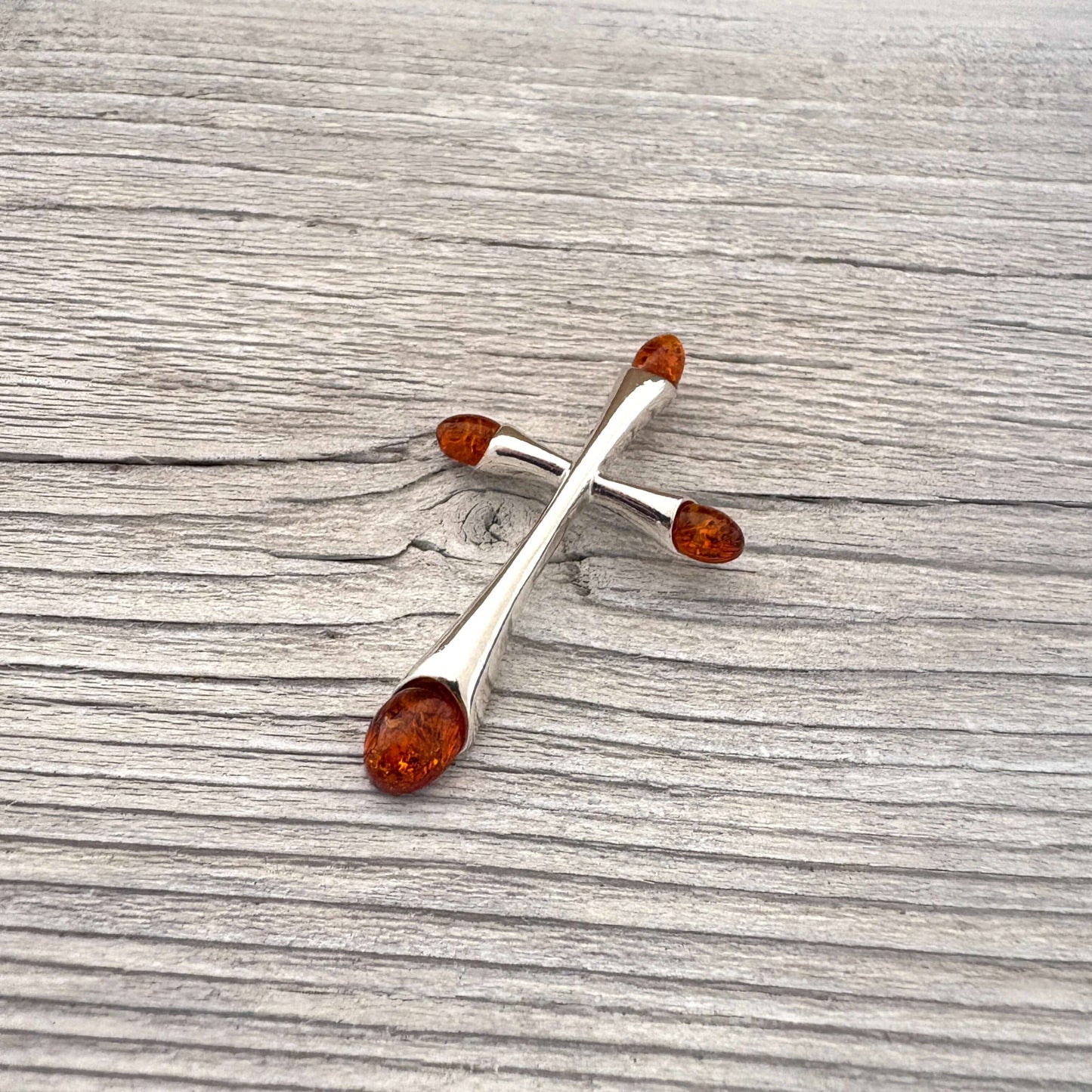 Silver cross-shaped brooch with amber stones on a wooden surface