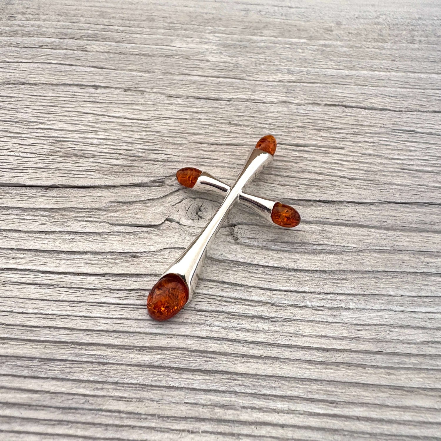 Silver cross-shaped brooch with amber stones on a wooden surface