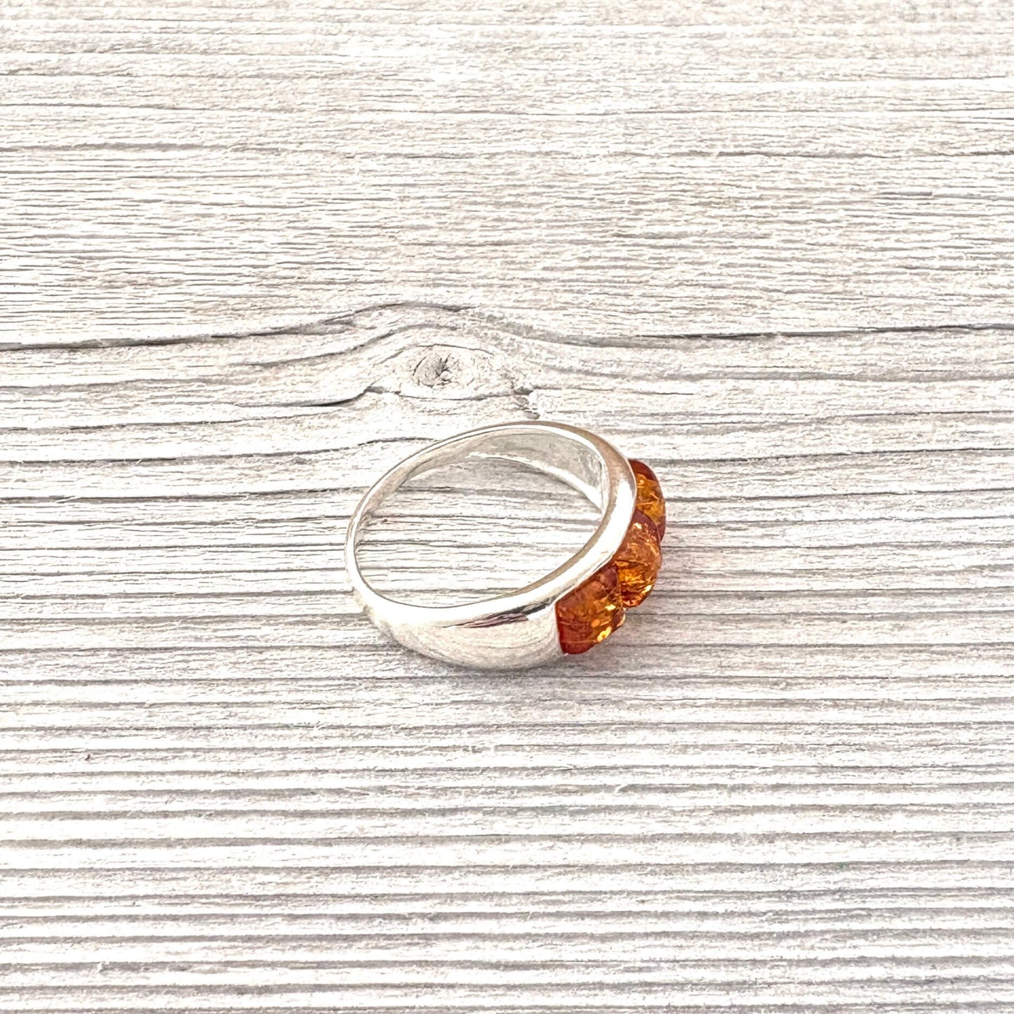 Silver ring with three square amber stones on a wooden surface