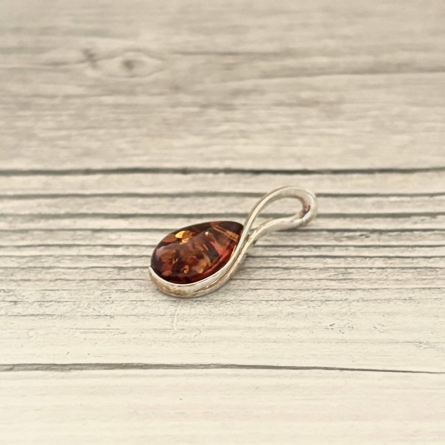 Teardrop shaped amber pendant set in sterling silver on a silver chain against a wooden background