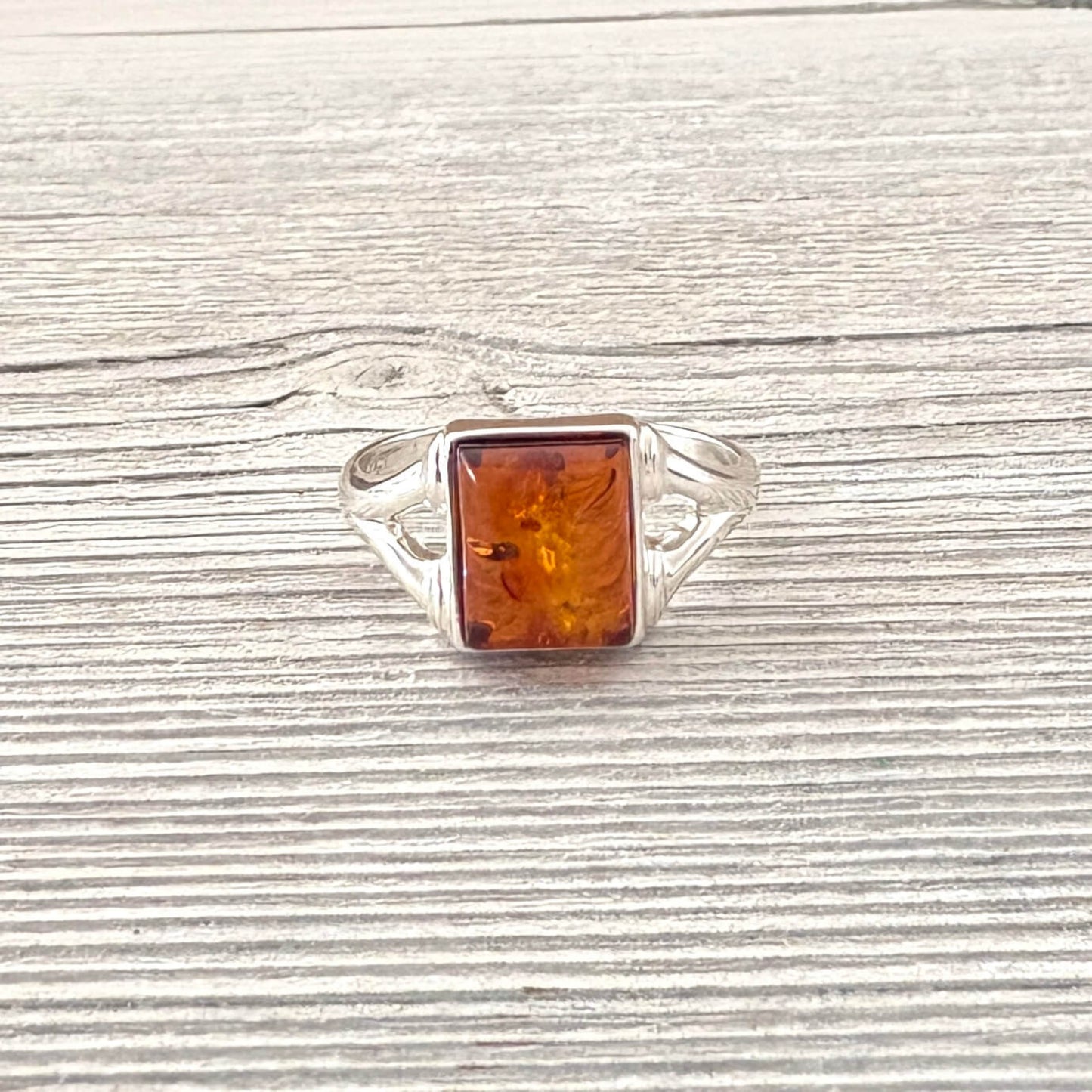 Silver ring with a rectangular amber stone on a wooden surface