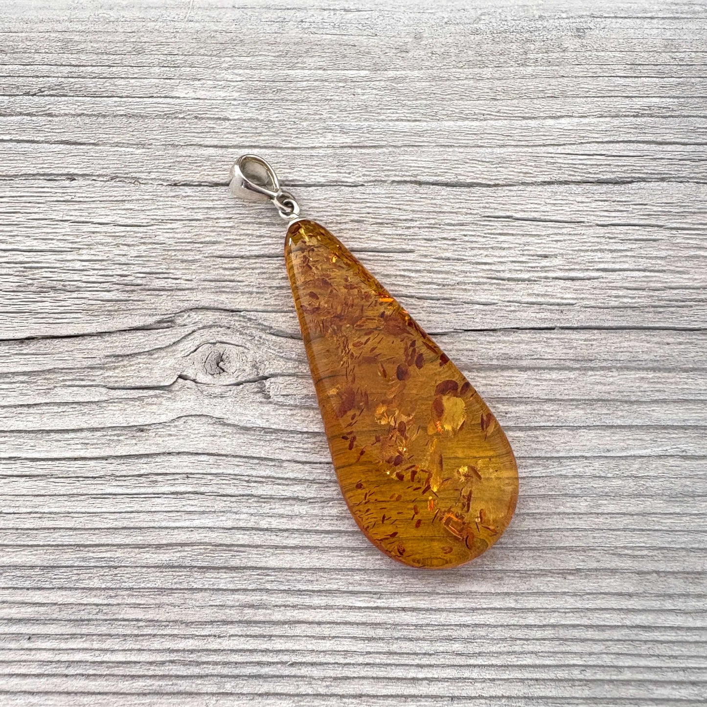 Left side teardrop-shaped amber pendant on with a silver bail against a wooden background