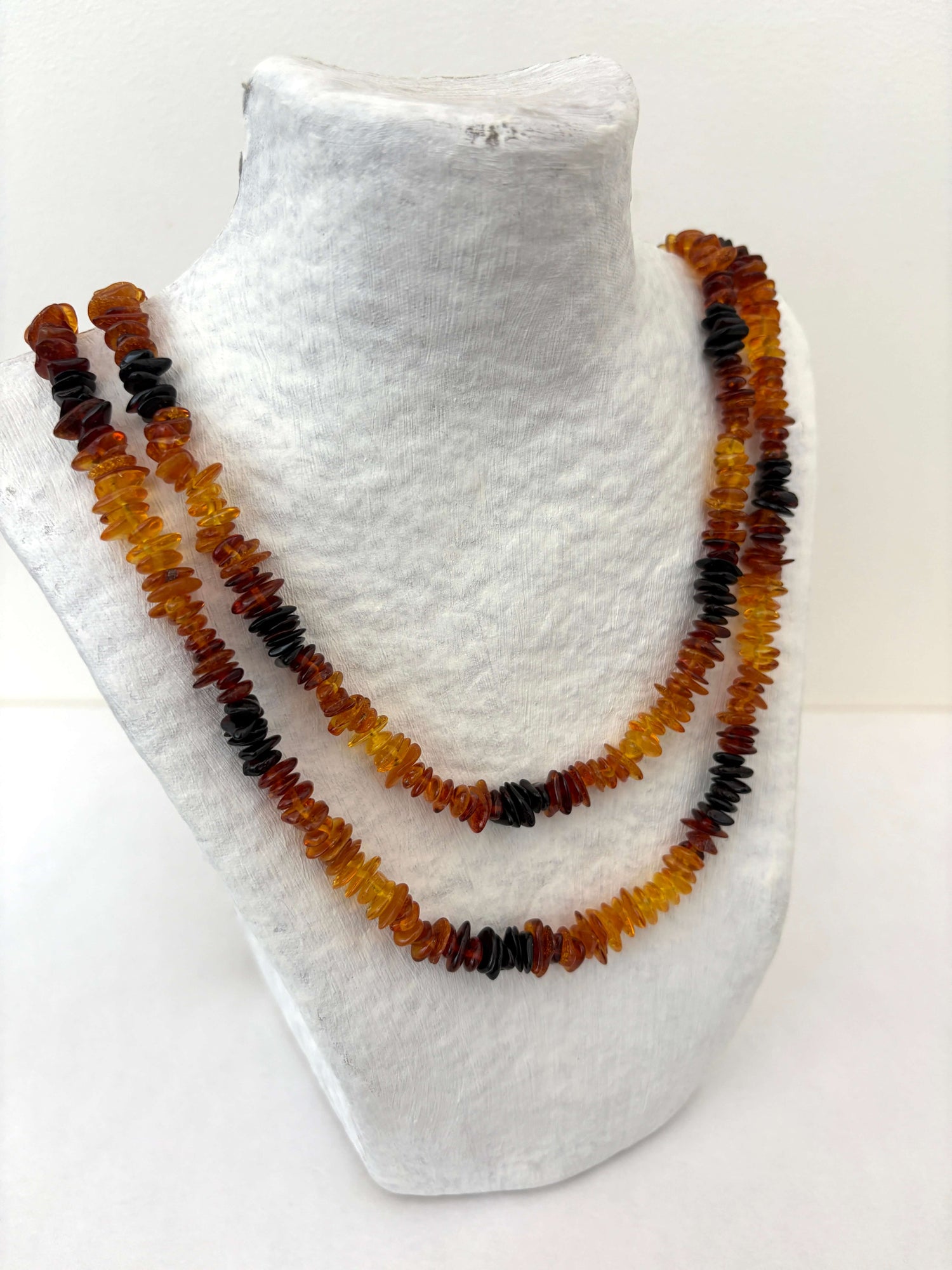 Layered amber necklace on a white mannequin bust.