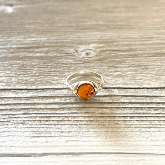 Silver ring with a round amber stone on a wooden surface
