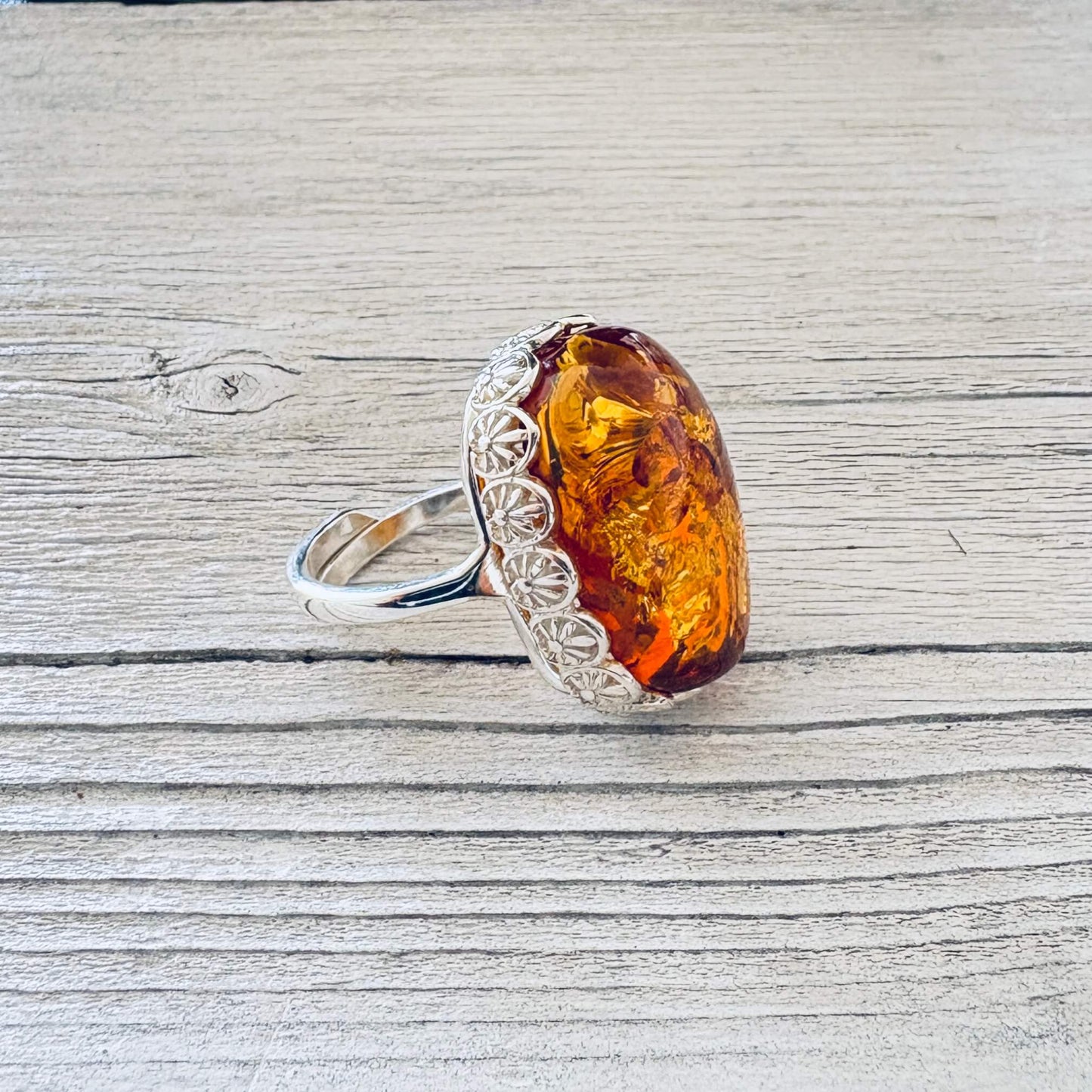 Side view of an oval Baltic amber ring featuring decorative silver floral detailing and an adjustable sterling silver band.