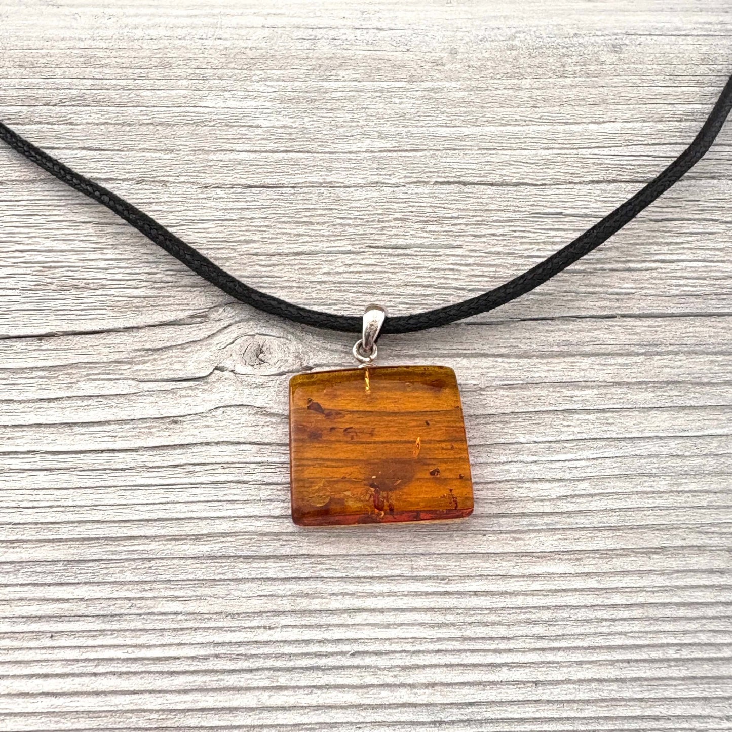 Necklace with a square wooden pendant on a black cord against a textured gray background