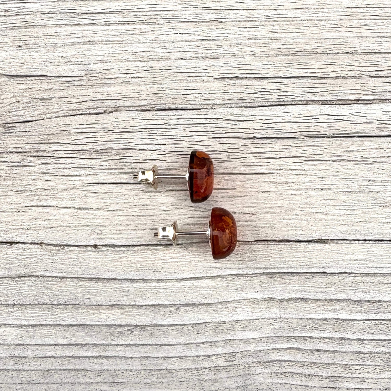 Pair of cognac amber oval shaped stud earrings on a wooden surface
