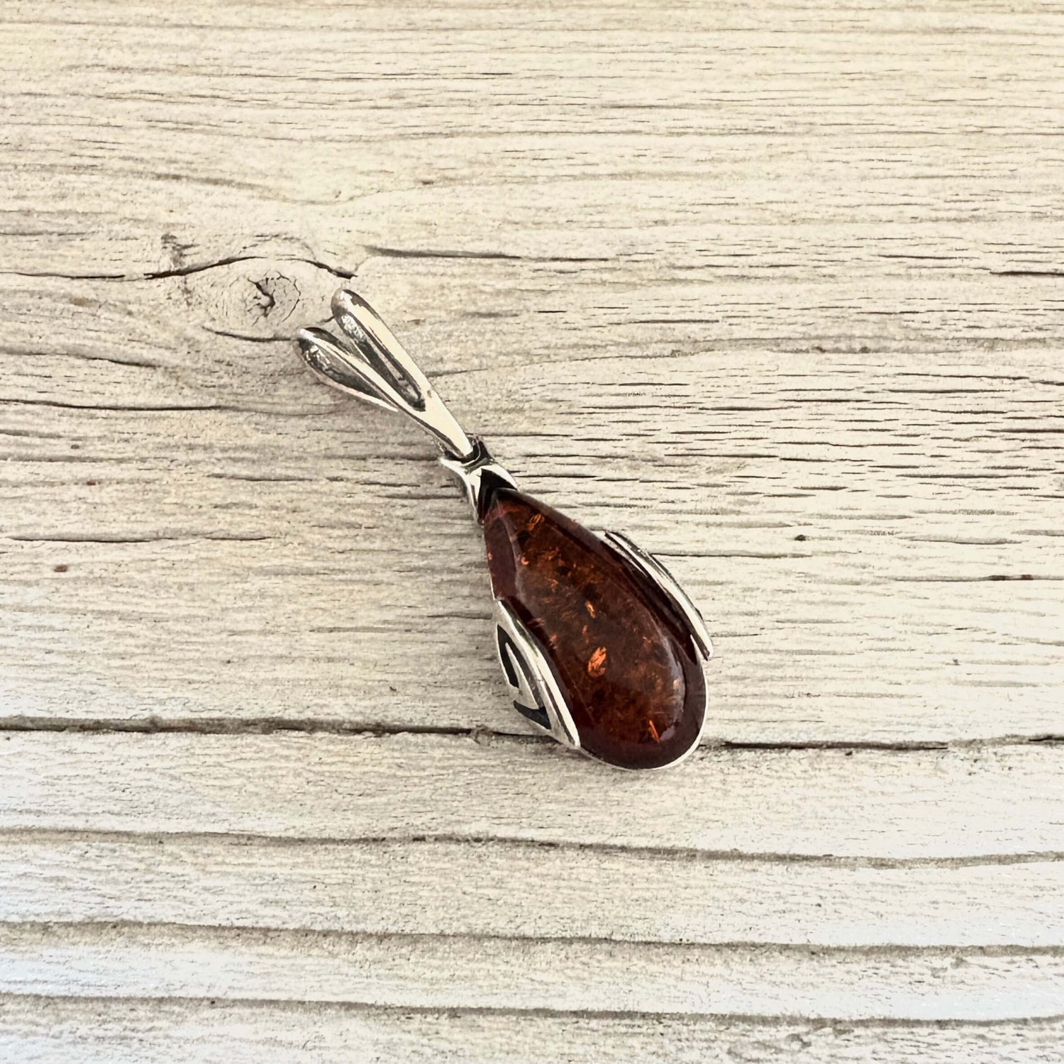 Angled view of cognac amber pendant. showing its curved silver setting, elongated teardrop shape and decorative detail.
