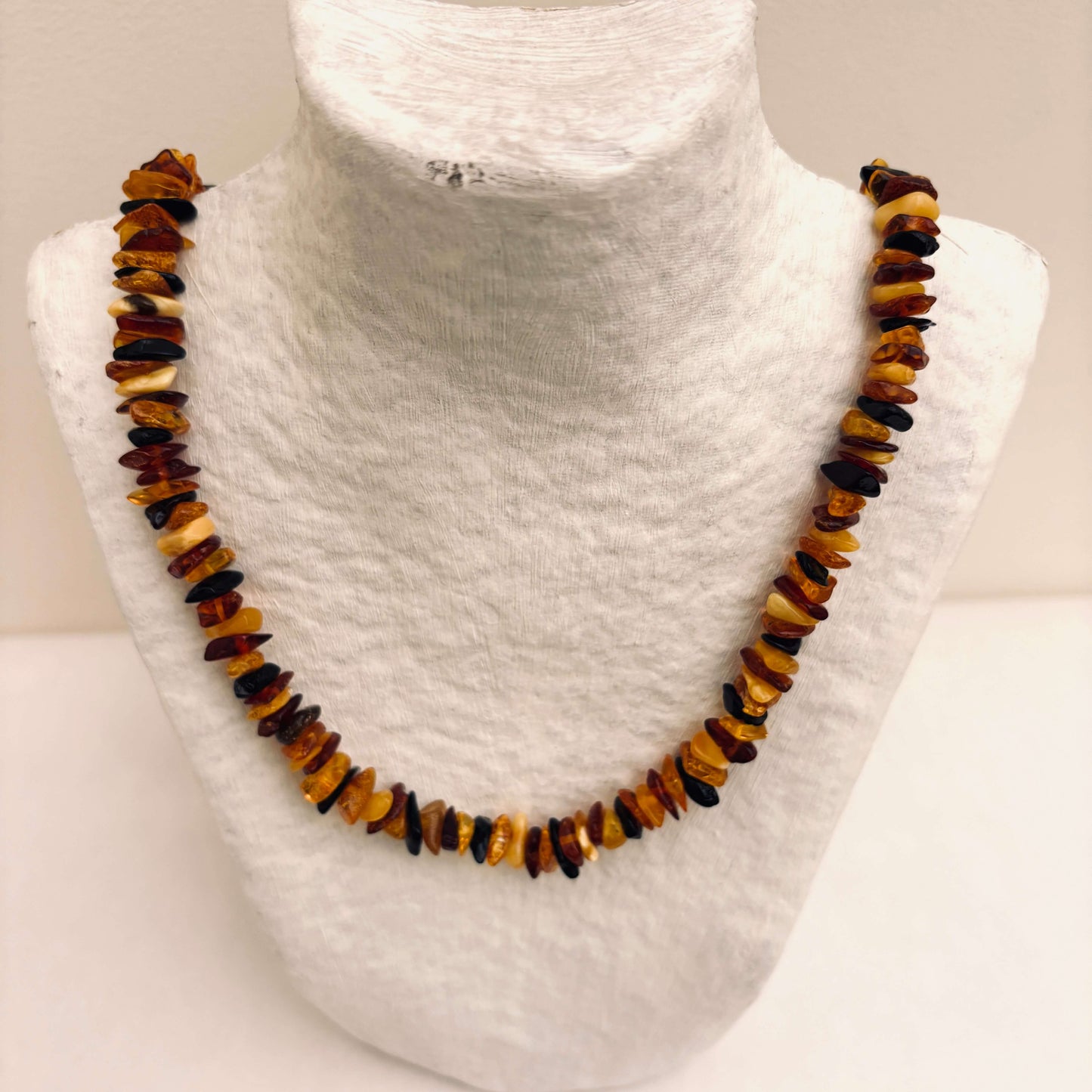 Necklace with multicolored amber beads on a mannequin neck.