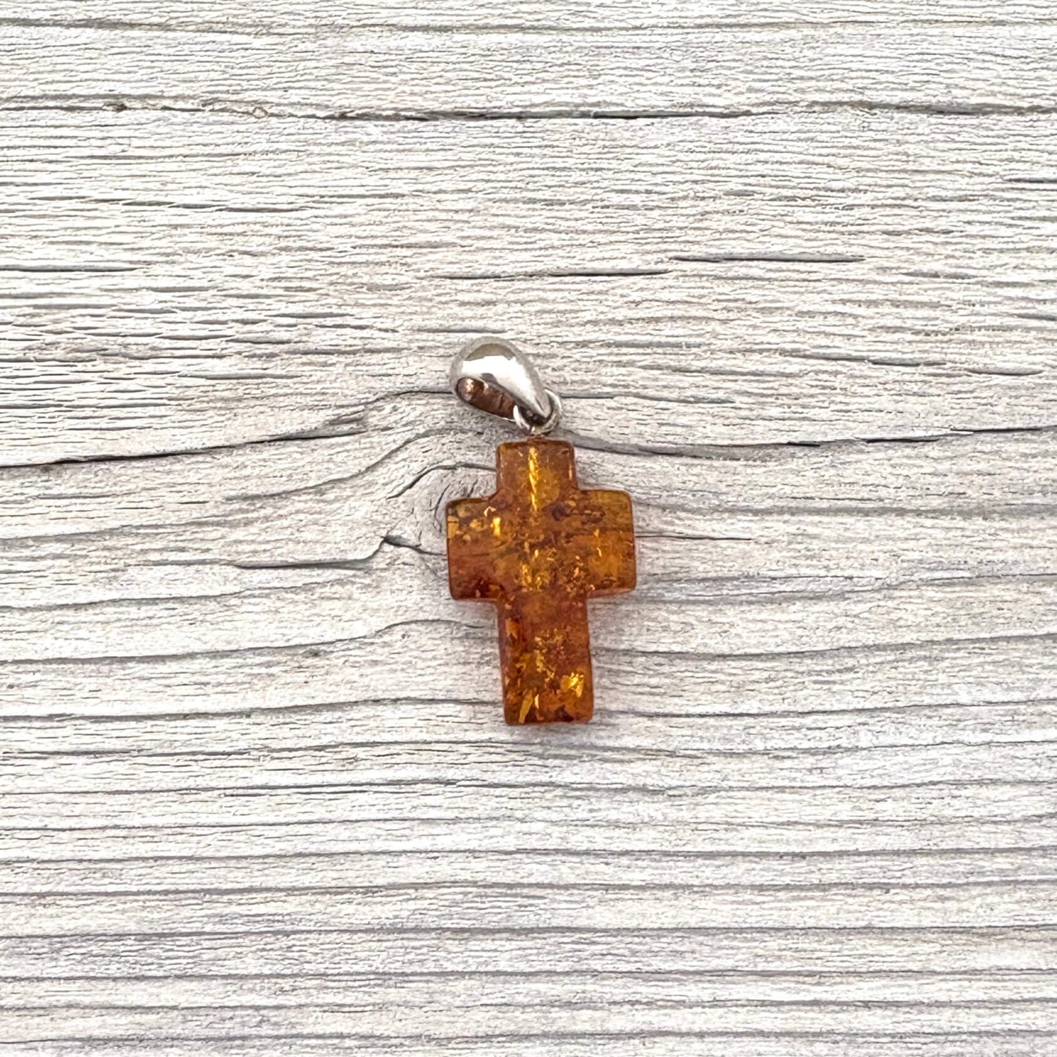 Amber cross pendant with a silver bail against a wooden background