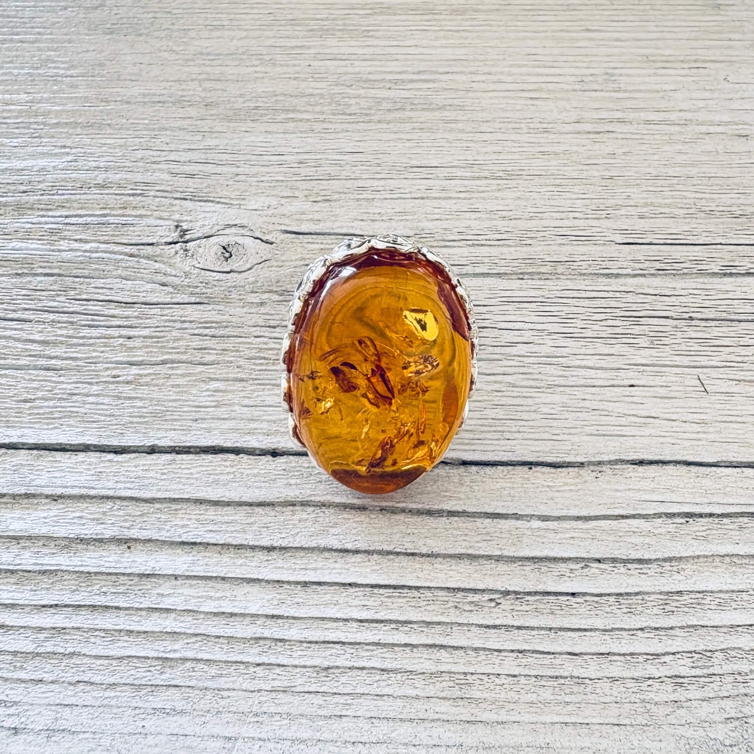 Oval honey cognac Baltic amber statement ring with intricate floral sterling silver edging, photographed from the front.