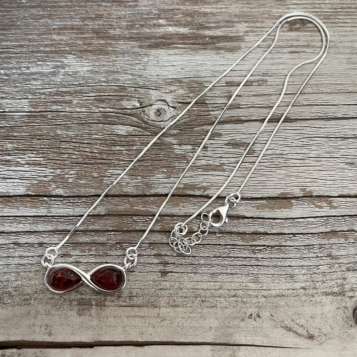 infinity shaped pendant with amber set in sterling silver on a silver string 