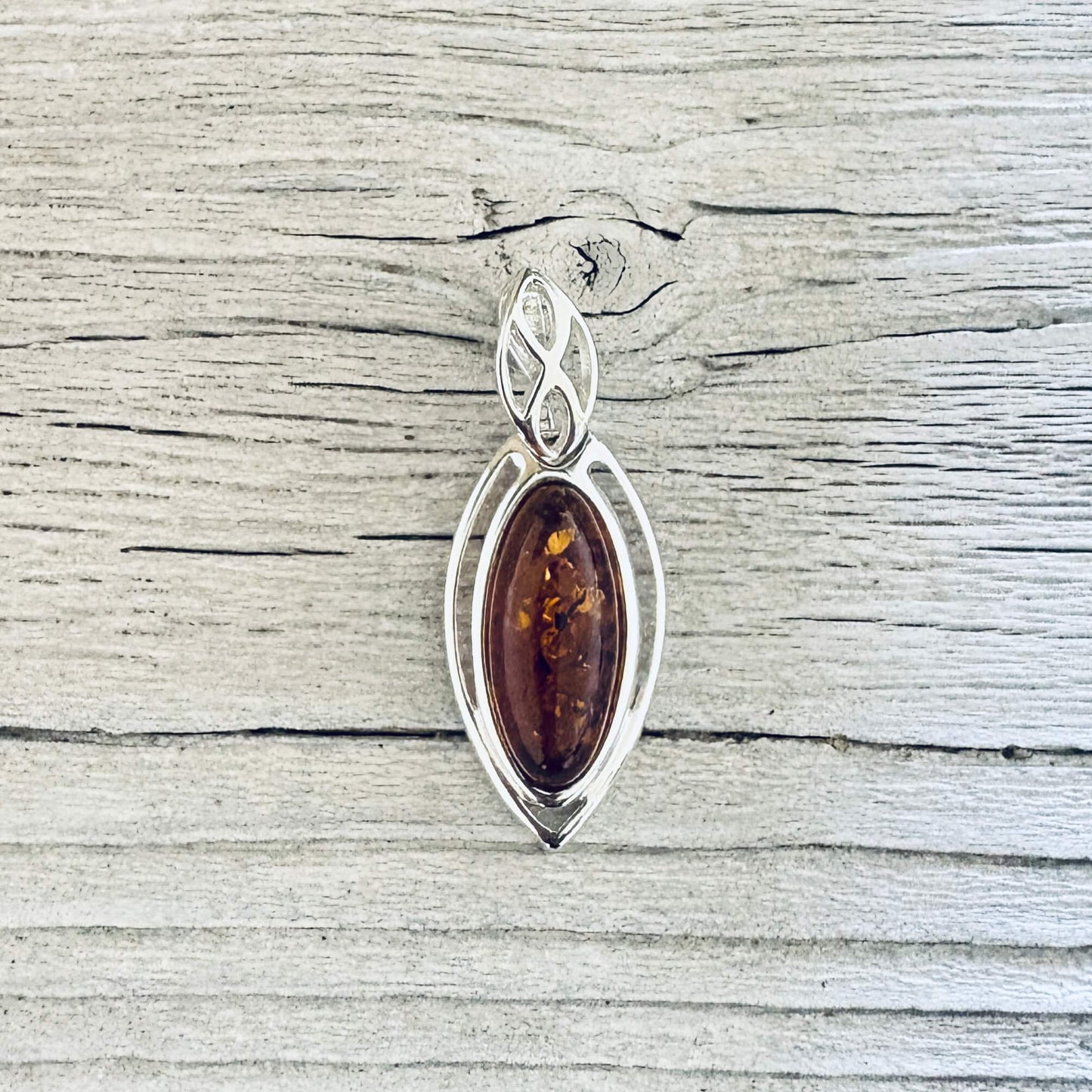 Cognac Baltic amber marquise pendant in a polished silver frame with decorative leaf style bail.