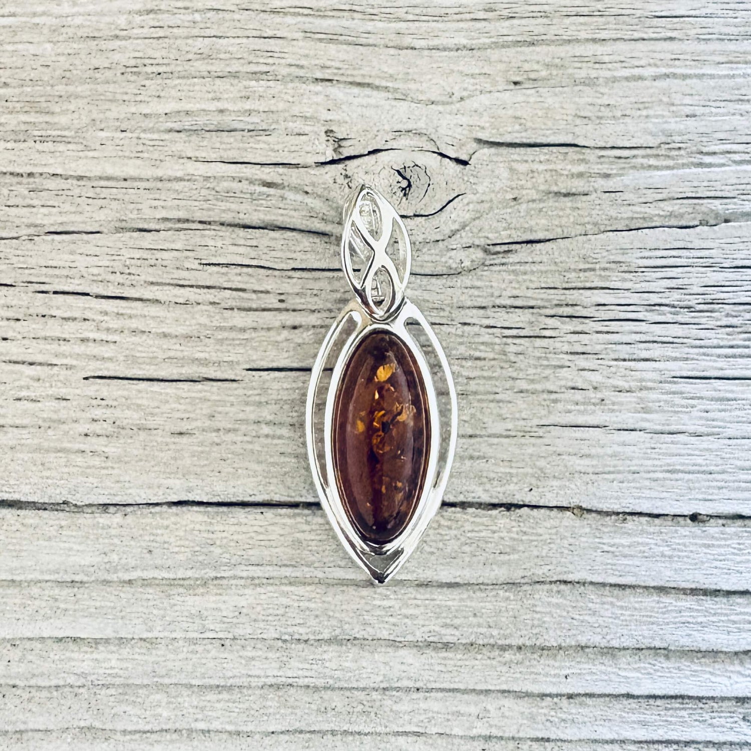 Cognac Baltic amber marquise pendant in a polished silver frame with decorative leaf style bail.