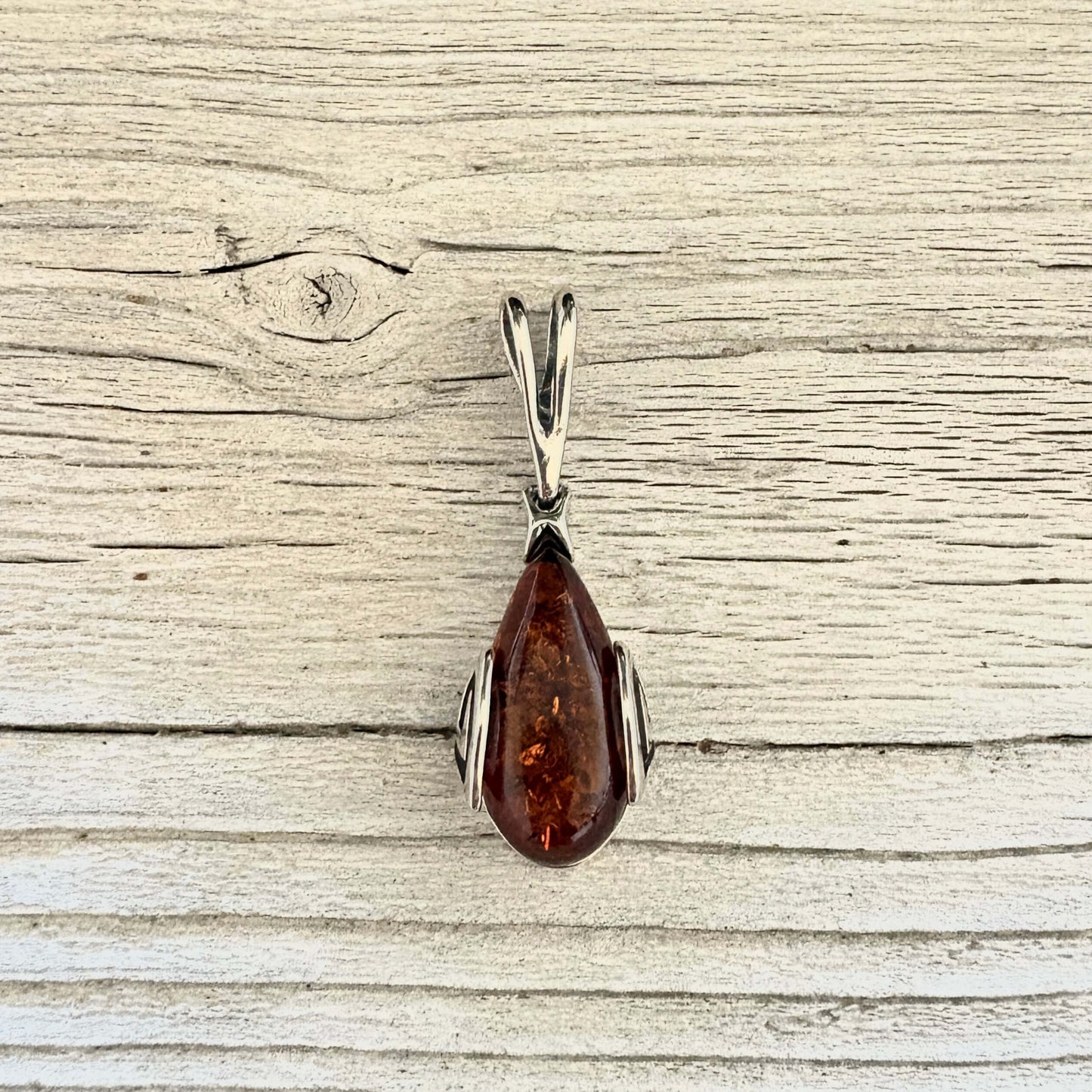 A teardrop-shaped amber pendant with a silver-toned metal setting.