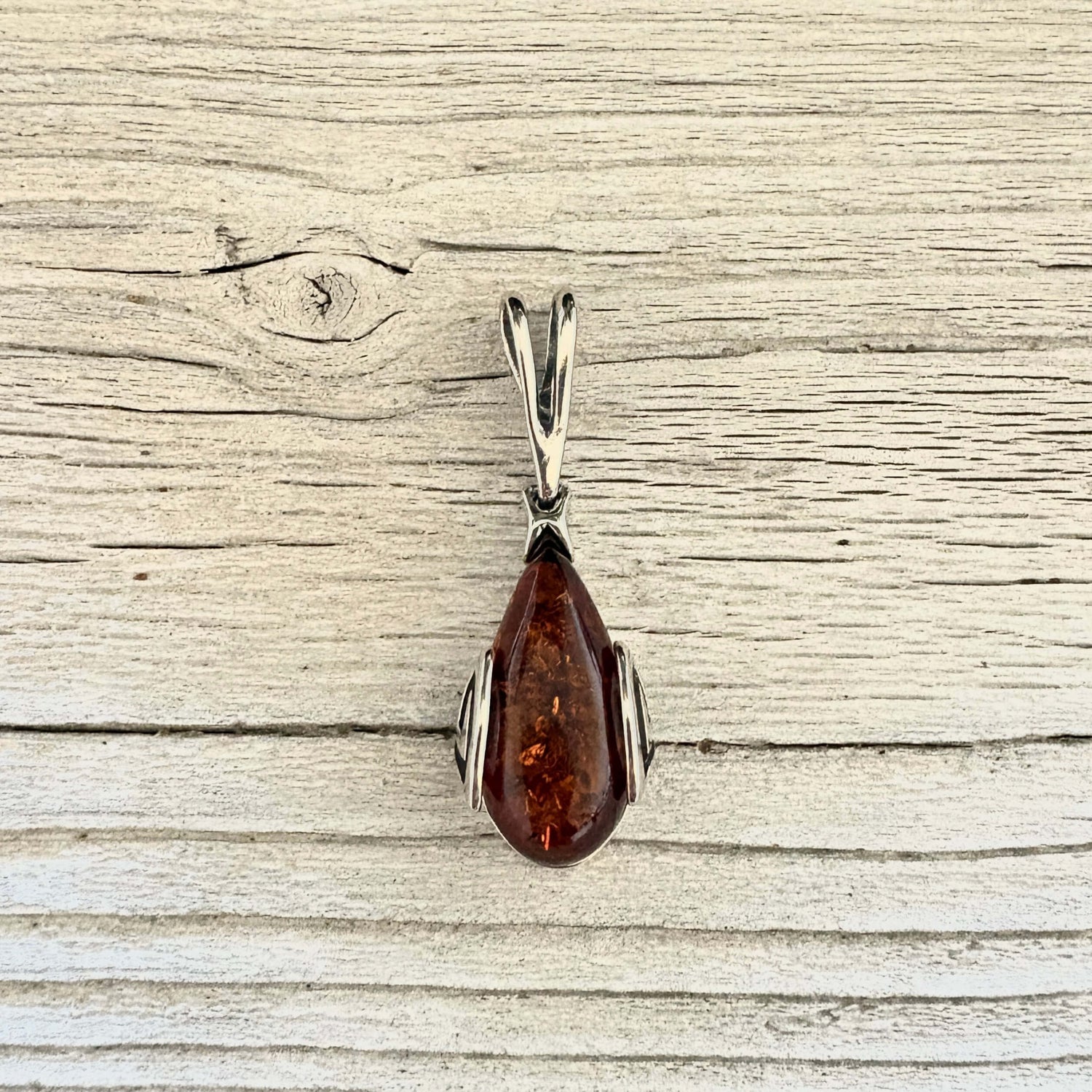 A teardrop-shaped amber pendant with a silver-toned metal setting.