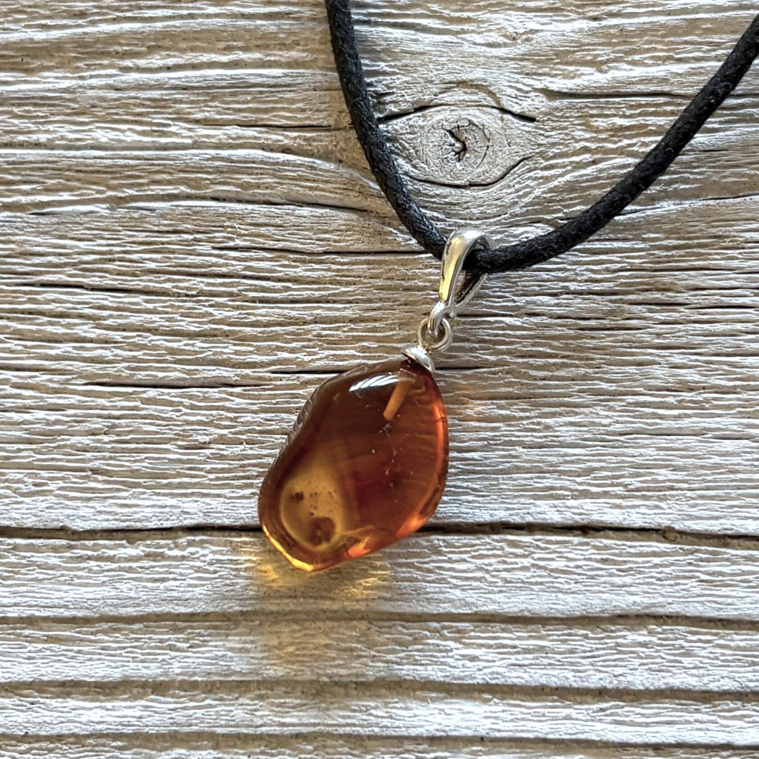 Amber pendant on a black cord against a wooden background