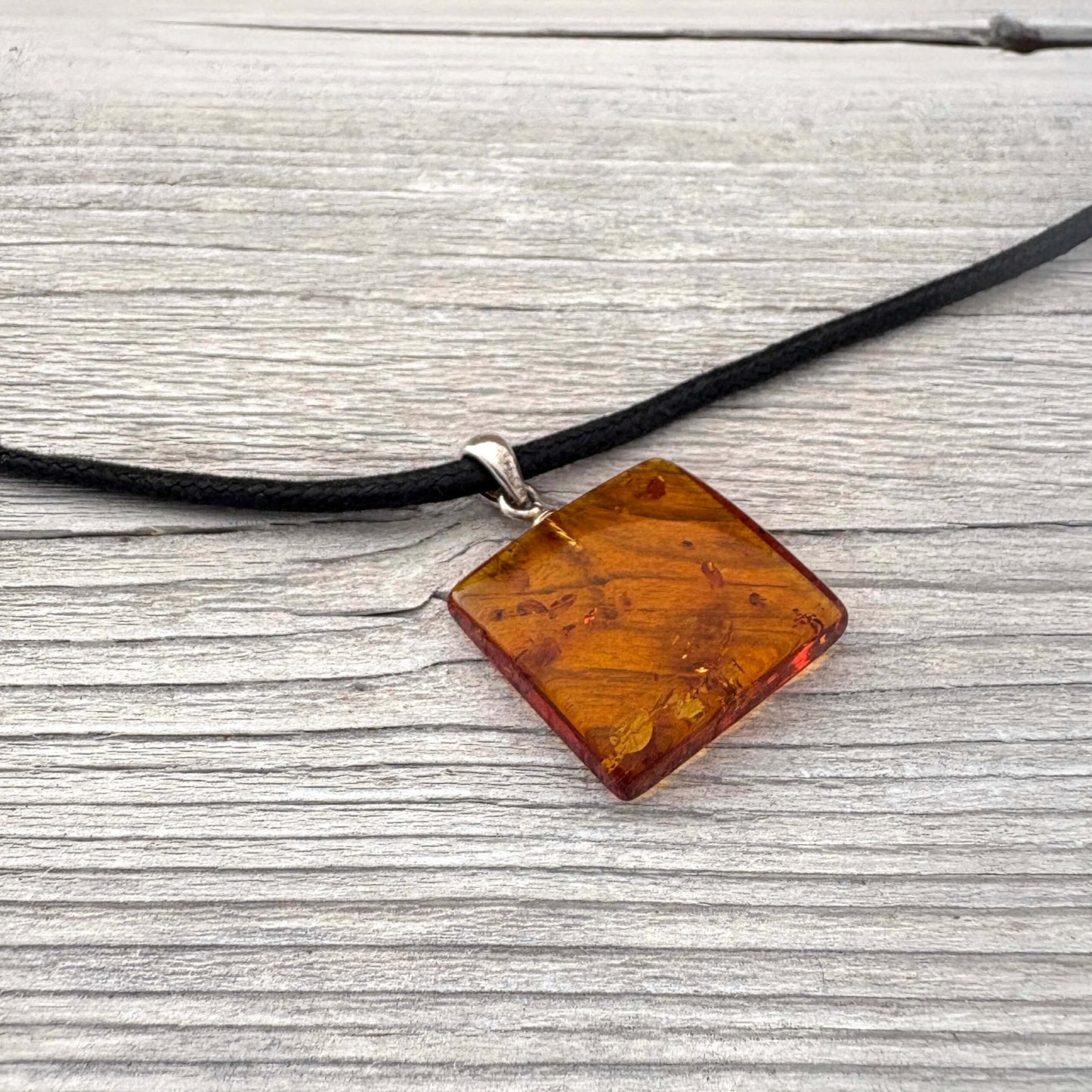 Necklace with a square amber pendant on a black cord against a wooden background