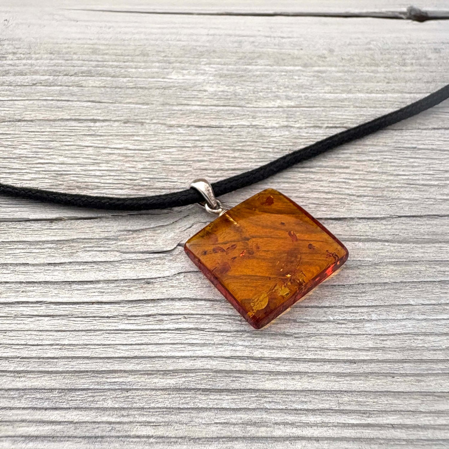 Necklace with a square amber pendant on a black cord against a wooden background