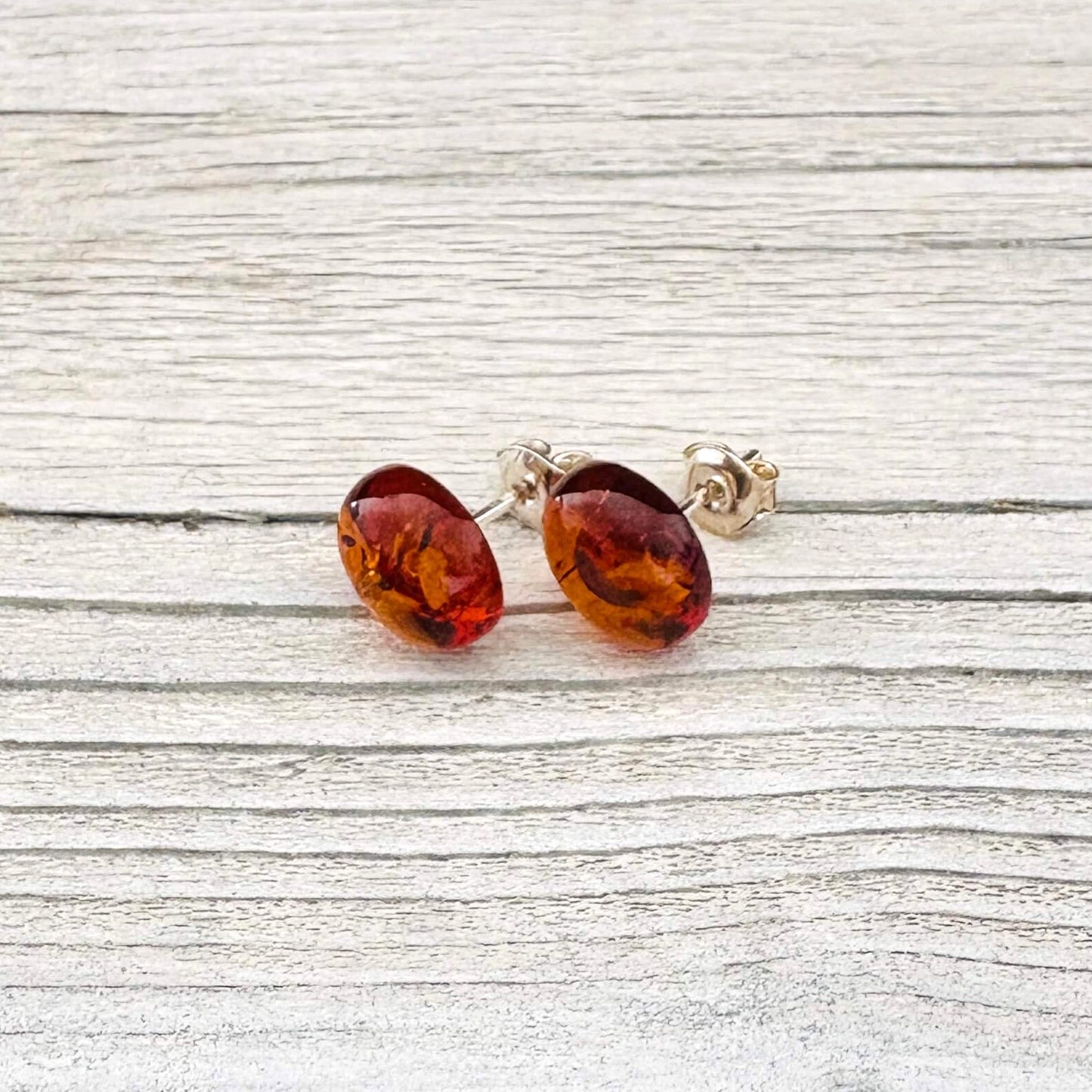 Pair of oval shaped amber stud earrings on a light wooden surface