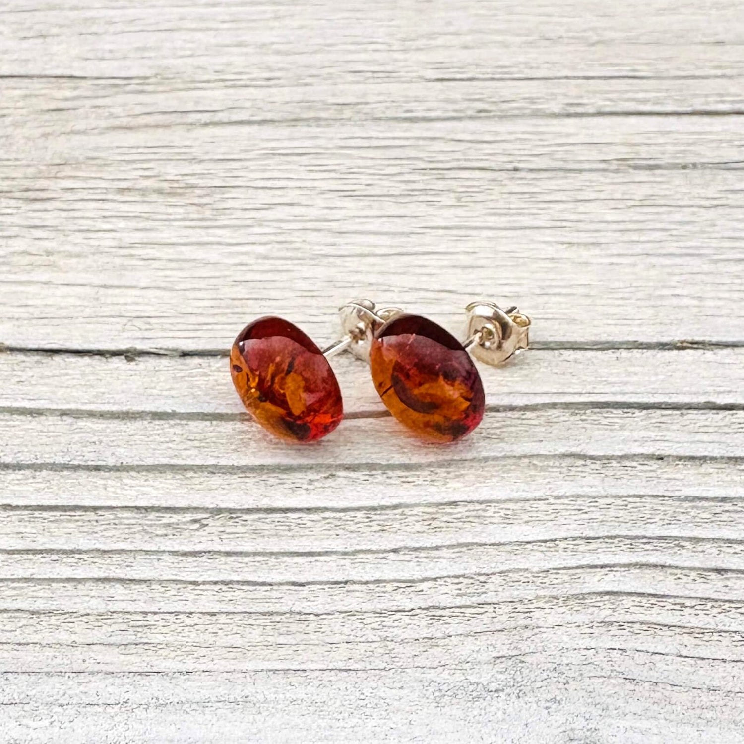 Pair of oval shaped amber stud earrings on a light wooden surface