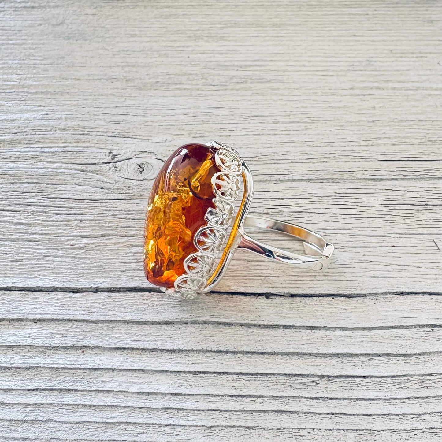 Adjustable sterling silver Baltic amber ring showing the raised oval honey cognac stone and ornate floral setting.
