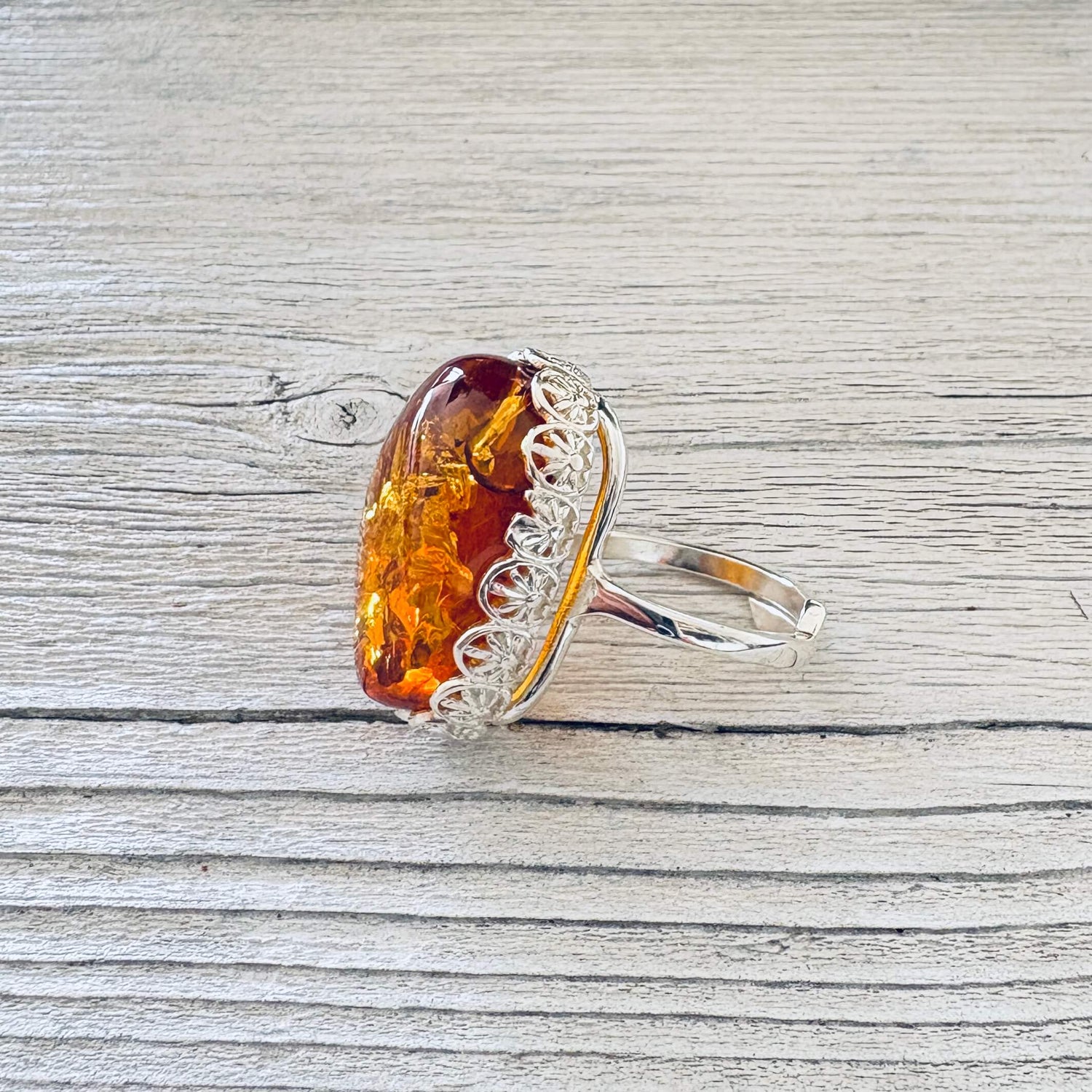 Adjustable sterling silver Baltic amber ring showing the raised oval honey cognac stone and ornate floral setting.