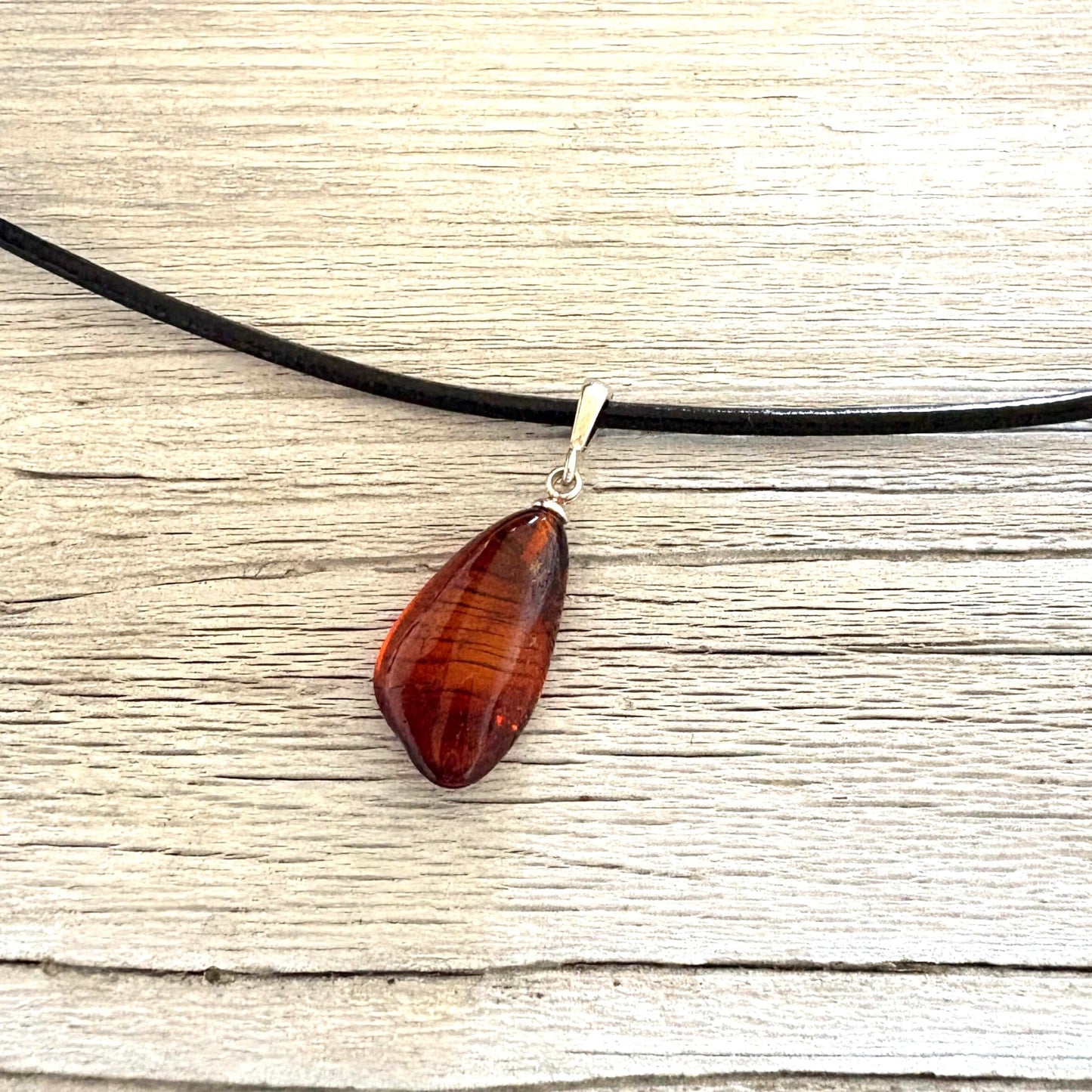Teardrop-shaped amber pendant on a black cord against a wooden background