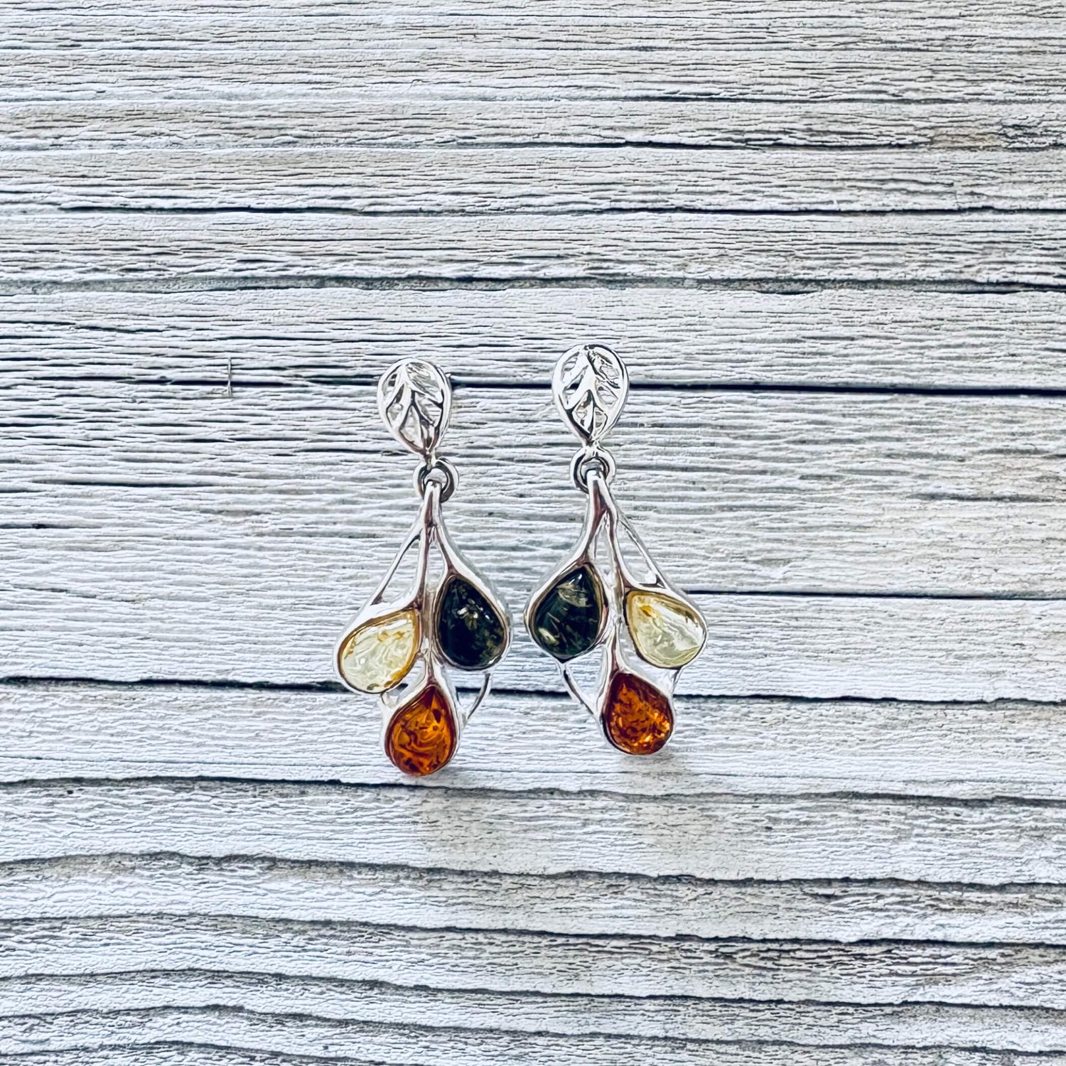 Pair of multicoloured Baltic amber earrings with three teardrop stones suspended in delicate silver branch style settings.