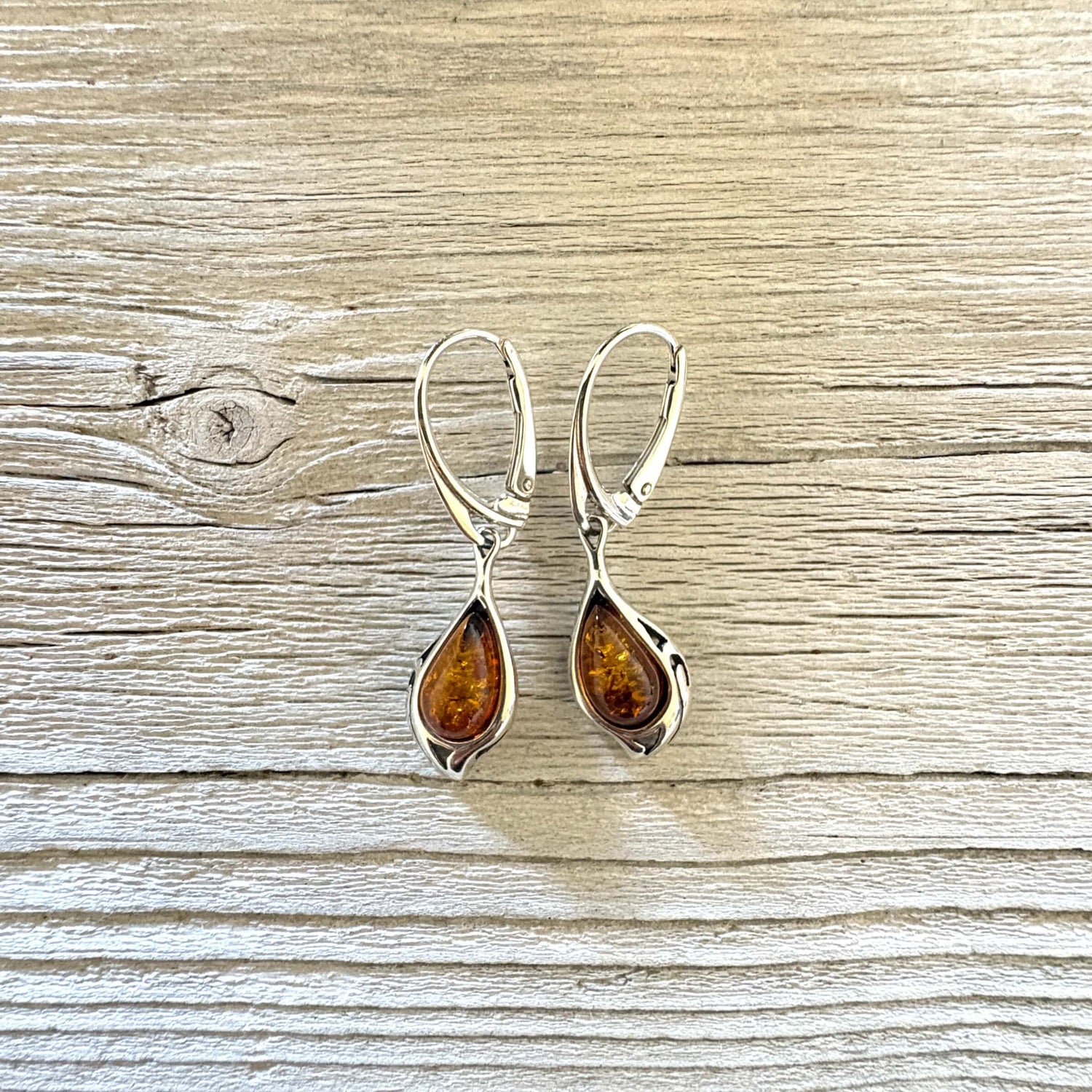 Cognac Baltic amber teardrop earrings framed by sculpted silver curves with elegant leverback hooks.