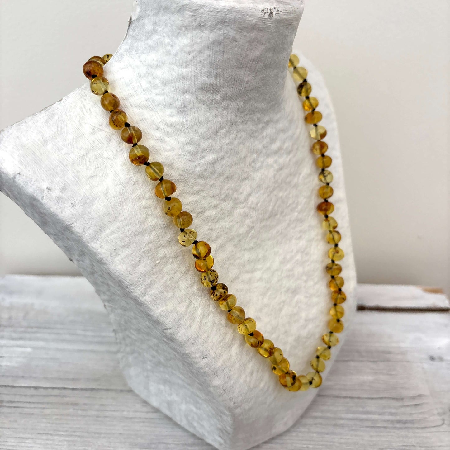 Beaded amber light green necklace on a mannequin bust with a neutral background