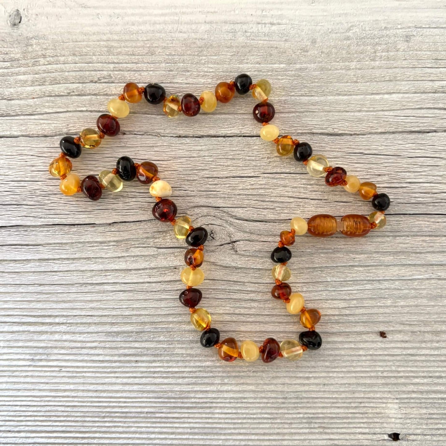 Multicolored beaded teething amber necklace on a textured wooden surface