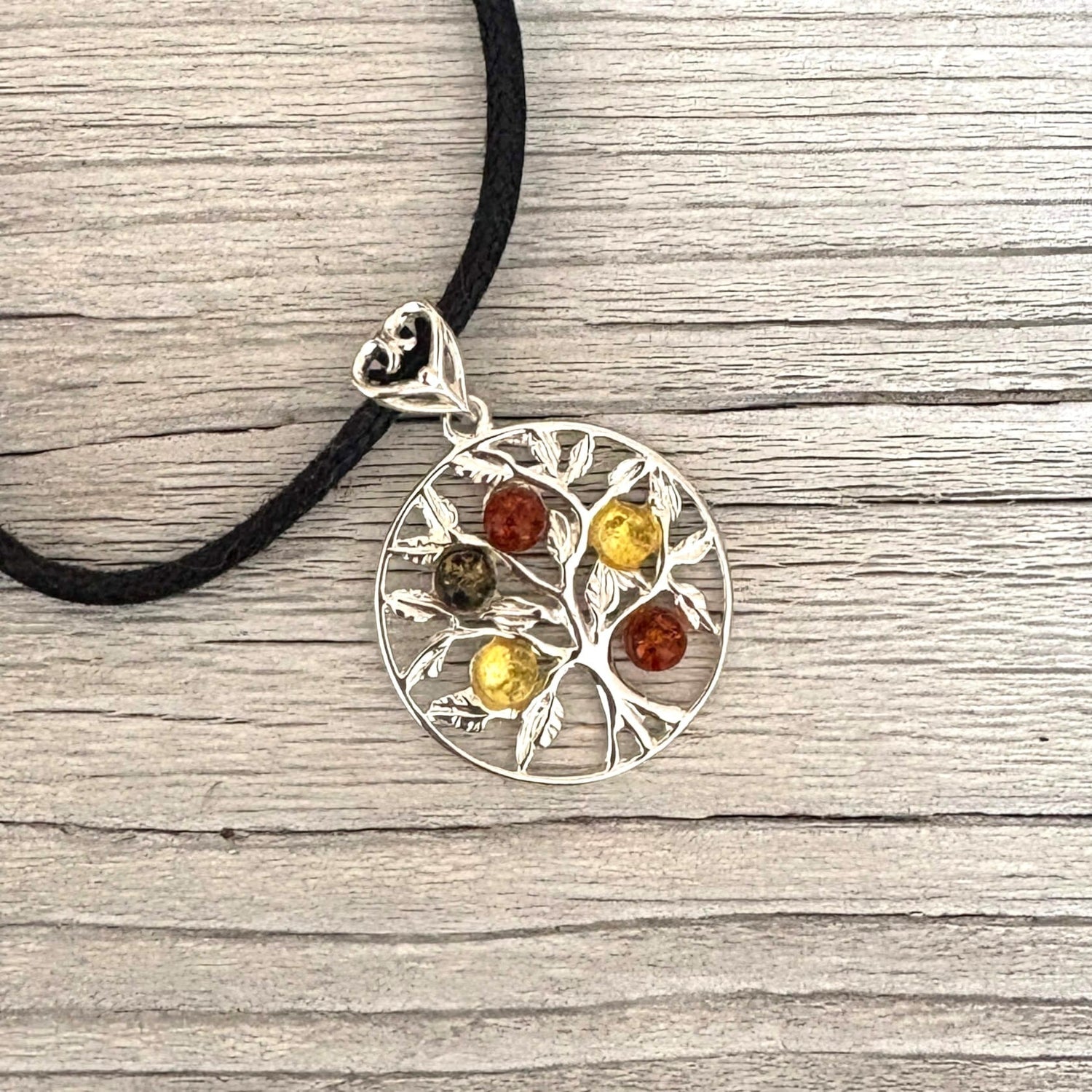 Silver tree-shaped pendant with colored stones on a black cord against a wooden background