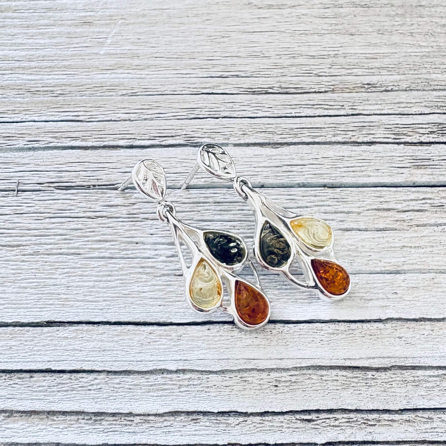 Angled green, honey and cognac Baltic amber drop earrings showing polished silver leaf detailing and butterfly back posts