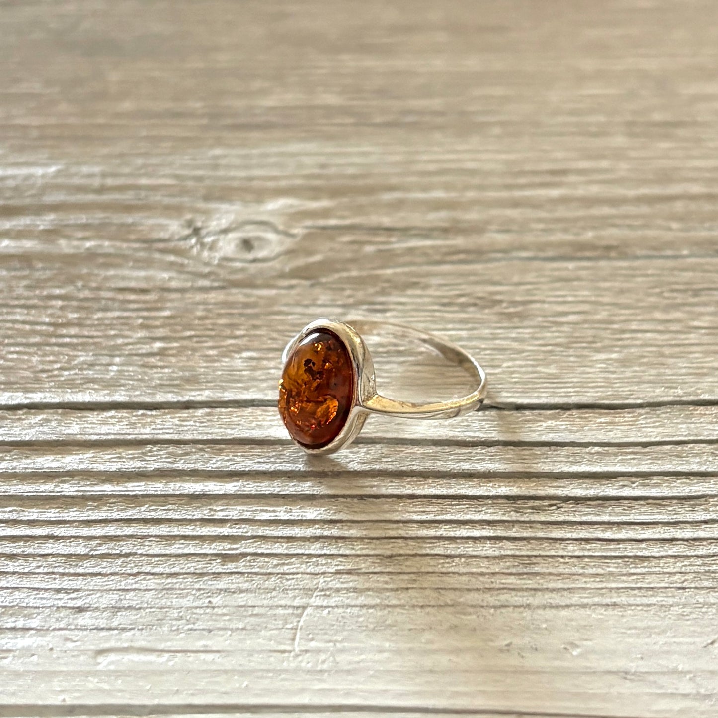 Silver ring with a oval shaped amber stone on a wooden surface