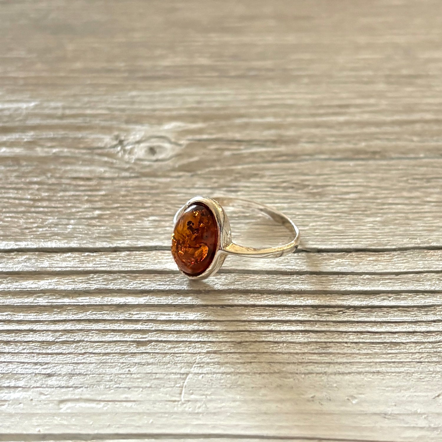 Silver ring with a oval shaped amber stone on a wooden surface