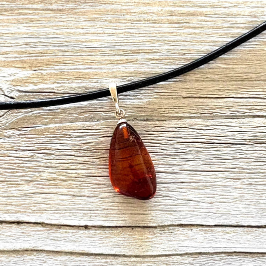 Teardrop-shaped amber pendant on a black cord against a wooden background