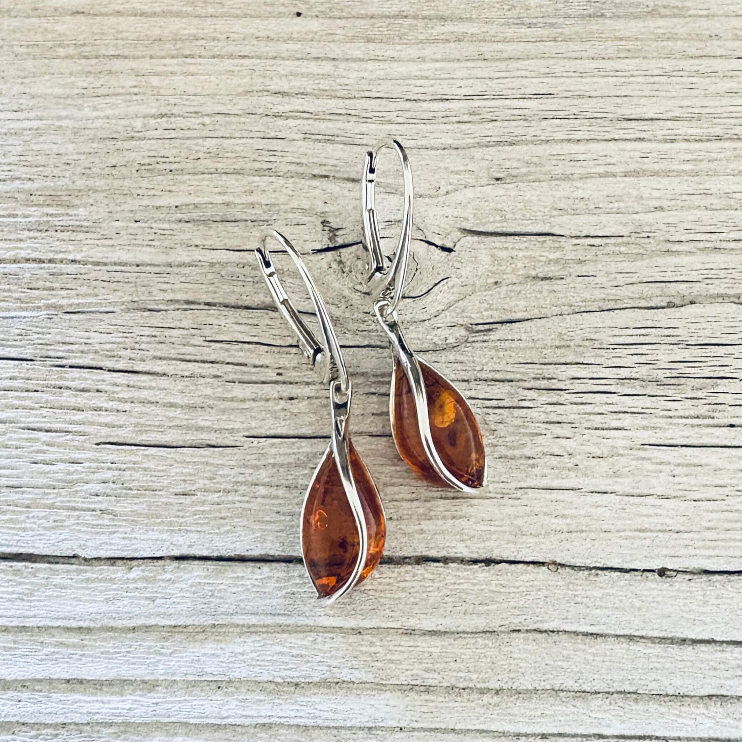 Elegant cognac amber teardrop earring featuring curved silver detailing and polished lever back closures.
