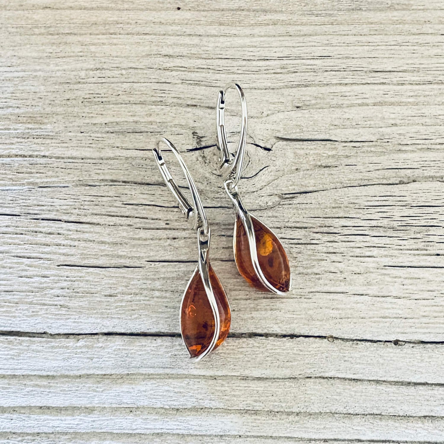 Elegant cognac amber teardrop earring featuring curved silver detailing and polished lever back closures.